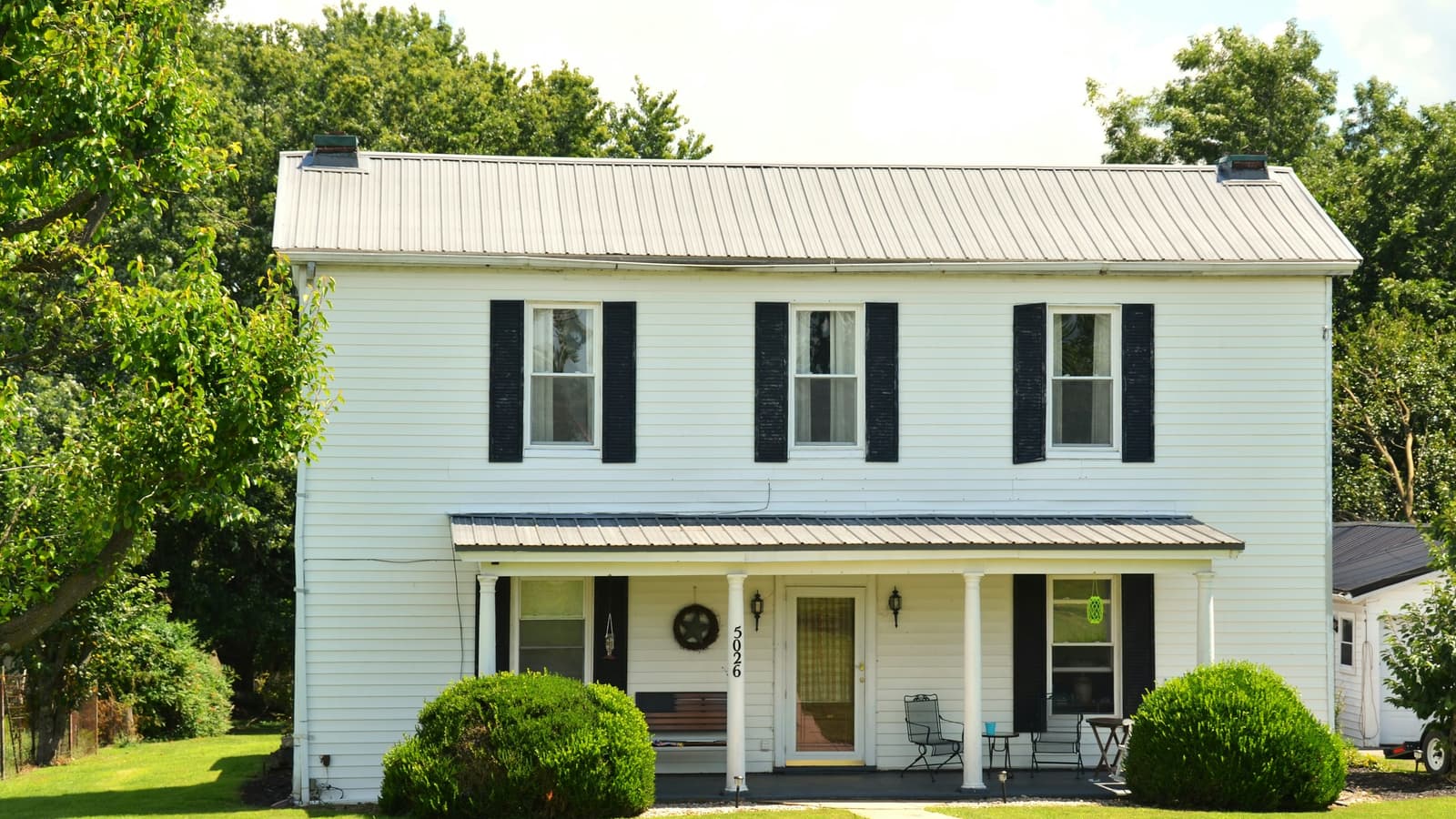 White two-story farmhouse-style home with black shutters, metal roof and a neatly mowed lawn